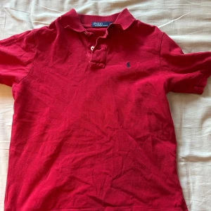 Röd pikétröja från Ralph Lauren - Säljer en klassisk röd pikétröja från Ralph Lauren. Tröjan har korta ärmar och en liten broderad logotyp på bröstet. Perfekt för en stilren och avslappnad look.