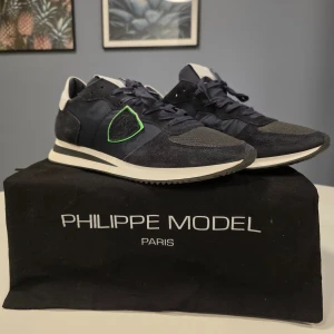 Philippe Model sneakers i blå mocka - Snygga Philippe Model sneakers i blå mocka med vita och svarta detaljer. Skorna har en grön broderad logga på sidan och snörning framtill. Perfekta för en stilren look.