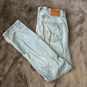 Ljusa jeans från Levis 501 - Säljer ett par ljusa jeans från Levis med klassisk femficksdesign och en brun läderpatch baktill. De har en straight passform och är perfekta för en avslappnad stil. Passar bra till sneakers och t-shirt. Som ni ser på bilden är de på gränsen på mig att de är för små, men ville endå visa någorlunda hur dem sitter. (Inte lika tajt som på mig) 