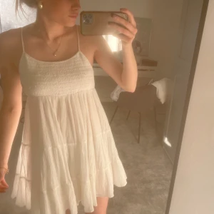 Vit ärmlös klänning - Säljer en söt vit ärmlös klänning med smala axelband och volangdetaljer. Perfekt för varma sommardagar. Klänningen har en luftig passform och är gjord i ett lätt material.