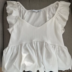 Vit volangtopp från Vero Moda - Säljer en söt vit topp från lager 157 med volangdetaljer vid axlarna och en v-ringad halsringning. Använd max 3 ggr🫶🏼