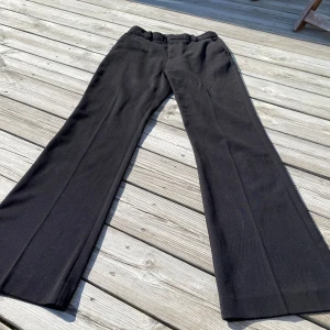 Svarta kostymbyxor från Lindex - Säljer ett par svarta kostymbyxor från Lindex med klassisk passform och raka, vida ben. Byxorna har fickor i sidorna och hällor för bälte. Perfekta för en stilren look.