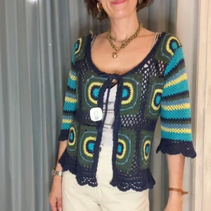 Färgglad virkad kofta med mönster - Säljer en unik virkad kofta med fyrkantiga mönster i blått, grönt, gult och turkost. Koftan har trekvartsärm och knytning framtill. Perfekt för dig som gillar retrostil och färg. Superfin över ett linne eller t-shirt!