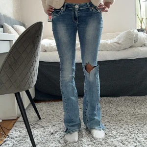 True Religion bootcut jeans blå - Säljer ett par blå bootcut jeans från True Religion med slitningar och hål på ena knät. Snygga kontrastsömmar och broderade bakfickor med orange detaljer. Klassisk femficksmodell och låg midja. Perfekta för dig som gillar en avslappnad och trendig look.