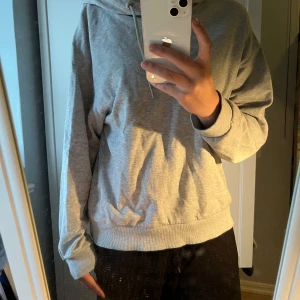 Grå hoodie från 157 - Säljer en enkel och stilren grå hoodie från 157 i storlek M, dock ganska liten i storlek. Tröjan har huva med dragsko och ribbade muddar vid ärmslut och nederkant. Perfekt för en avslappnad look.