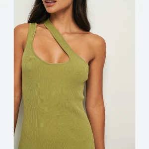 Grön klänning - Säljer en olivgrön ribbad klänning med oneshoulder-design och kroppsnära passform. Klänningen är ärmlös och har en unik asymmetrisk axelrem. 