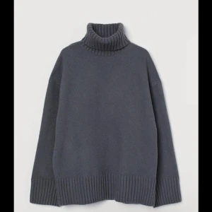 Mörkgrå stickad polotröja - Säljer en mörkgrå stickad polotröja med bred ribbstickad kant vid ärmslut, nederkant och krage. Tröjan har en oversized passform och långa ärmar, perfekt för kyliga dagar.