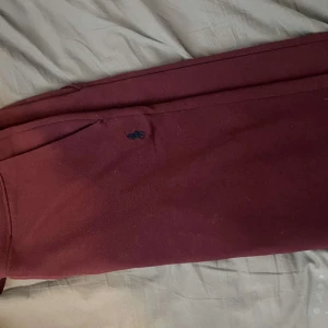 Vinröda mjukisbyxor Polo Ralph Lauren - Vinröda mjukisbyxor från Polo Ralph Lauren med broderad logga vid fickan. Byxorna har muddar vid bensluten och är tillverkade i mjukt bomullsmaterial. Perfekta för chill dagar eller när du vill vara bekväm men ändå se snygg ut.