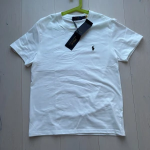 Vit t-shirt från Polo Ralph Lauren - Klassisk vit t-shirt från Polo Ralph Lauren med broderad logga på bröstet. T-shirten har rund hals och korta ärmar. Perfekt basplagg med stilren design.