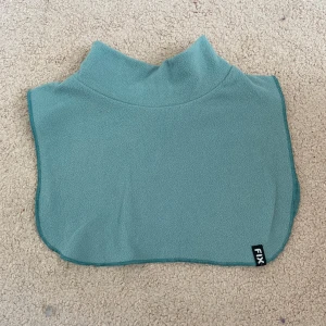 Ljusblå fleecehalsduk från FIX - Mjuk och smidig ljusblå fleecehalsduk från FIX med hög krage. Perfekt att dra över huvudet för extra värme. Passar barn i storlek 4-6 år. Enkel och stilren design utan mönster.