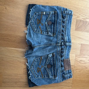 LTB jeansshorts stl 27  - Snygga blå jeansshorts från LTB med slitna kanter och råa avslut. Shortsen har bakfickor med broderade byxor detaljer och knappar, samt flätad detalj i midjan. .