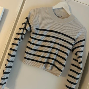 Randig ribbad tröja från 157 - Snygg ribbstickad tröja från 157 i vit med svarta horisontella ränder. Tröjan har rund halsringning, lång ärm och en croppad passform som ger en trendig look. Perfekt att matcha med jeans eller kjol för en chill stil.