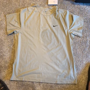 Ljusgrön Nike Dri-FIT t-shirt herr - Nypris 449kr. Storlek XL. Oanvänd, köpt på Intersport. Nike Dri-FIT t-shirt i ljusgrått med svart logga på bröstet. Tillverkad i funktionsmaterial som andas, perfekt för träning. Klassisk passform med korta ärmar och rund halsringning.