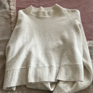 Krämvit stickad tröja från Lindex - Mysig krämvit stickad tröja från Lindex med ribbade muddar och hög hals. Perfekt för lager-på-lager och chill dagar. Tröjan har en relaxed fit och är superenkel att matcha med jeans eller kjol.