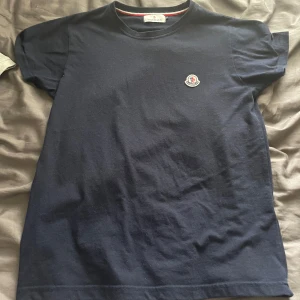 Mörkblå Moncler t-shirt  - Snygg mörkblå t-shirt från Moncler med klassisk passform och rund hals. T-shirten har ett broderat Moncler-logo på bröstet och är gjord i mjuk bomull. Perfekt för dig som gillar stilrena och exklusiva plagg.