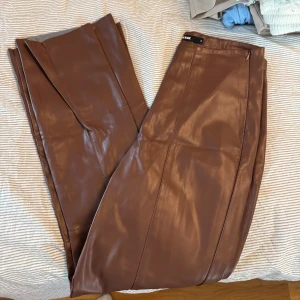 Bruna skinnbyxor från Bik Bok - Säljer ett par bruna skinnbyxor från Bik Bok i storlek S. Byxorna har hög midja och raka ben med sömdetaljer framtill. Kedja på sidan för att kunna öppna/stänga. Aldrig använda! 