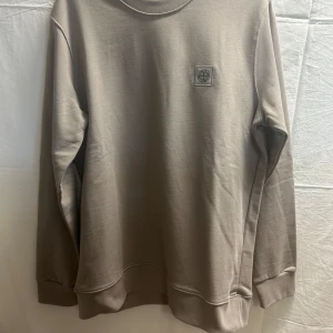 Grå sweatshirt från Stone Island - Snygg grå sweatshirt från Stone Island med klassisk rund hals och logopatch på bröstet. Tröjan är i mjuk bomull och har långa ärmar samt ribbade muddar. 