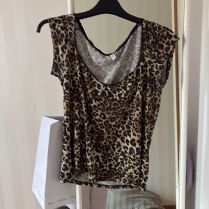 Leopardmönstrad topp från Nelly XL - Snygg topp från Nelly i storlek XL med leopardmönster i bruna, svarta och beige toner. Modellen har korta armar med djup rundad ringning och svarta spetsdetaljer längs halsen. Jättefin på sommaren! 🩷