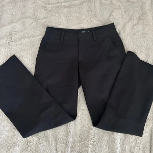 Svarta kostymbyxor - Klassiska svarta kostymbyxor från BikBok i storlek 34. Byxorna har utsvängda ben, hällor för bälte och sidfickor. Perfekta för en clean och stilren look.  Modell Vera