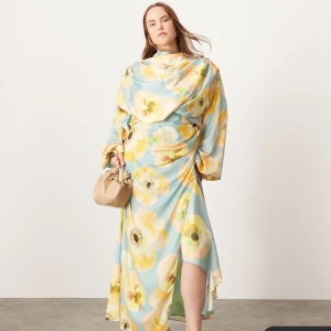Blommig långklänning med draperad hals - Säljer en långklänning med stort blommönster i gult och grönt på ljusblå botten. Klänningen har draperad hals, långa ärmar och figurnära midja. Perfekt för dig som vill sticka ut med en färgglad och elegant look.