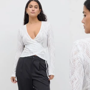 Gina vit topp - Säljer en vit omlottopp i spets med lång ärm och v-ringning. Toppen har ett fint spetsmönster och knyts i sidan för en snygg passform. Perfekt att styla med både byxor och kjol. OANVÄNDA nypriset 359kr