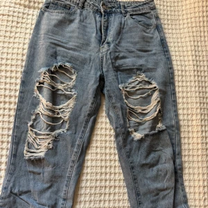 Ljusblå ripped jeans från SHEIN - Säljer ett par ljusblå jeans från SHEIN med stora slitningar över båda knäna. Jeansen har klassisk femficksdesign, normal passform och stängs med dragkedja och knapp. Perfekta för en avslappnad och trendig look.