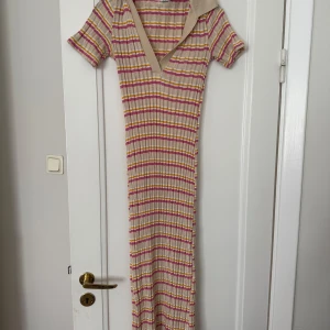 Randig ribbad långklänning med v-ringning - Säljer en lång, ribbad klänning med korta ärmar och v-ringning. Klänningen har ett randigt mönster i beige, rosa och gula toner. Från Zara!