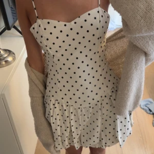 Vit prickig kortklänning med smala axelband - Supersöt vit kortklänning med svarta prickar och smala axelband. Klänningen har en figurnära passform upptill och volangig kjol nedtill. Perfekt för sommarens alla tillfällen! Materialet känns lätt och luftigt. Den är helt oanvänd då jag fick 2 stycken!❤️❤️❤️ Pris är såklart inte fast!