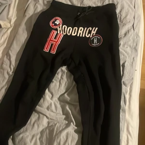 Svarta mjukisbyxor från Hoodrich - Svarta mjukisbyxor från Hoodrich med tryckta loggor och stora bokstäver framtill. Byxorna har dragsko i midjan och är perfekta för en avslappnad stil. Snygga detaljer med patchar och tryck på benen.