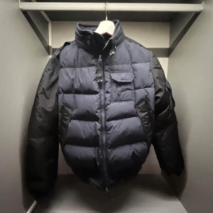 Mörkblå dunjacka från Parajumpers - Säljer en mörkblå Parajumpers dunjacka i storlek medium. Jackan har quiltad design, hög krage och dragkedja framtill. Fodrad med 90/10 dun, flera fickor och coola detaljer som orange insida och märkets logga. Perfekt för kalla dagar och riktigt snygg streetstil.