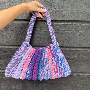 Handgjord virkad  axelväska i lila och blåa nyanser - Unik axelväska som är virkad för hand i flera färger som lila, rosa och blå. Väskan har en chunky känsla och bred axelrem, perfekt för dig som vill sticka ut med en färgglad accessoar. Väskan är 36cm bred och 18 cm hög