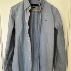 Ljusblå skjorta från Ralph Lauren - Klassisk ljusblå skjorta från Ralph Lauren med button-down krage och broderad logga på bröstet. Skjortan är i väldigt fint skick. Nypris ca 1600. Hör av er vid frågor!