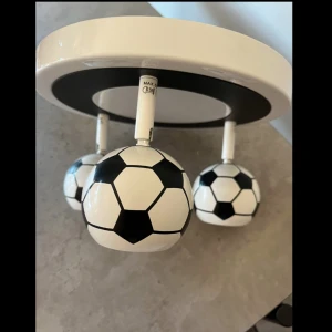 Taklampa med fotbollstema - Säljer en rund taklampa i vitt och svart med tre justerbara spotlights formade som fotbollar. Lampan är tillverkad i metall och plast och passar perfekt till barnrummet eller för den fotbollsintresserade. Monteras direkt i taket. Köpt för 1500kr