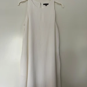Klänning, Massimo Dutti, 40, vit - Vit klänning med rund halsringning och ärmlös design från Massimo Dutti. Storlek 40. Klänningen har en nyckelhålsöppning med knapp i nacken och diskreta fickor i sidorna. Den har en avslappnad A-passform och en subtil textur. Tjockare material med undertyg, därav ej genomskinlig. Klänningen är i nyskick. Innertyg/foder 100% viskos. Yttertyg 98% viskos och 2% elastan.   Mått: Längd ca 86 cm Byst ca 46 cm Midja ca 55 cm