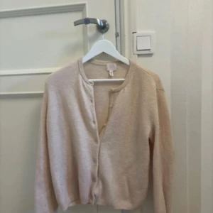 Ljusbeige kofta från H&M - Mysig ljusbeige kofta med rund hals och knappar framtill. Tröjan är stickad och har långa ärmar. Perfekt för lager-på-lager och enkel att matcha med olika outfits.