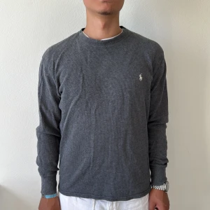 Mörkgrå långärmad tröja från Polo Ralph Lauren - Säljer en mörkgrå långärmad tröja från Polo Ralph Lauren med liten vit broderad logga på bröstet. Tröjan har en klassisk passform och är tillverkad i mjuk bomull. Perfekt för en stilren och avslappnad look.