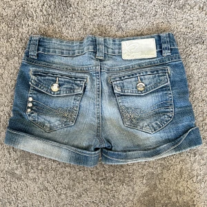 Blå jeansshorts från WeTweens by KappAhl - Snygga vintage blå jeansshorts från WeTweens by KappAhl med uppvikta benslut och dekorativa bakfickor med broderade detaljer och knappar. Klassisk femficksmodell och normal passform. Perfekta för varma dagar! Dom är också låg/medel i midjan. Skriv privat om du har frågor! Pris kan diskuteras💕Midjemåttet är 32 rakt över💗