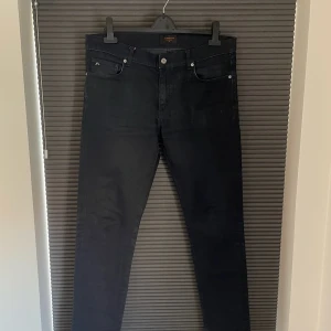 Marinblå  jeans från J.Lindeberg - Slimfit jeans från J.Lindeberg med klassisk femficksdesign och diskret logga på myntfickan. Jeansen har normal midja och smal passform. Storlek 34/34