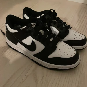 Nike Dunk Low svartvita sneakers - Säljer ett par Nike Dunk Low sneakers i svart och vitt. Skorna har snörnings, rund tå och platt sula. Perfekta för dig som gillar stilrena och tidlösa sneakers med ikonisk design.