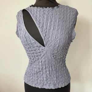 Lila ärmlös topp - Säljer en ljuslila ärmlös topp med vågig struktur och unik asymmetrisk öppning på ena axeln. Toppen har en tight passform och är tillverkad i ett stretchigt syntetmaterial. Storlek M och är aldrig använd!💜