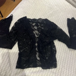 Svart spetsblus med knappar - Säljer en svart blus i genombruten spets med långa ärmar och knappar framtill. Blusen har en spetsdetalj och skit fin fest tröja!🤩