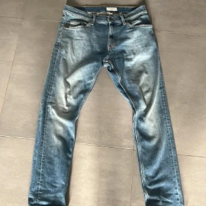 Blå slim fit jeans från tiger of Sweden - Säljer ett par klassiska blå slim fit jeans med fem fickor och dragkedja. Jeansen har en snygg tvättad look och sitter tajt längs benen. Perfekta till sneakers och t-shirt för en clean vardagsstil. Storlek 30:30