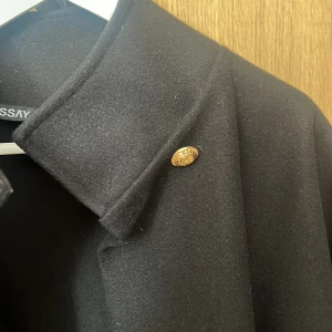 Svart kappa med hög krage från missay - Stilren svart poncho jacka från missay med hög krage och en snygg  guldig knapp vid halsen. Så snygg, använt ett par gånger så den är så gott som ny!