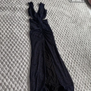 Glittrig marinblå bal/fest långklänning med slits - Säljer en marinblå långklänning med glittrigt tyg och djup v-ringning. Klänningen har en snygg slits framtill och är figurnära upptill. Perfekt för festliga tillfällen när du vill sticka ut.