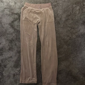 Beige mjukisbyxor från Juicy Couture - Säljer ett par beige mjukisbyxor från Juicy Couture med bred resår i midjan och snörning. Byxorna har raka ben, två fickor fram och två bakfickor med knappar. Supermjuka och perfekta för en avslappnad stil.