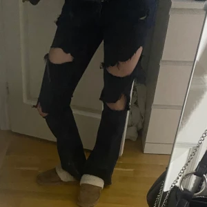 Mörkblå slitna low waist bootcut jeans - Säljer ett par mörkblå jeans med stora slitningar över knän och lår. Jeansen har normal passform och bootcut nertill, klassisk femficksmodell och knappgylf. Perfekta för dig som gillar en edgy och avslappnad stil. Pris går att diskutera