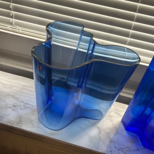 Blå Alvar Aalto vas från Iittala - Säljer en ikonisk blå Alvar Aalto vas från Iittala. Vasen har en organisk, vågformad design och är tillverkad i blått glas. Perfekt som inredningsdetalj eller för blommor. Klassisk skandinavisk design.