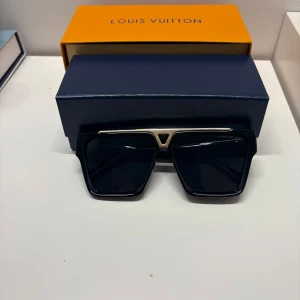 Louis Vuitton glasögon - Stilrena svarta solglasögon från Louis Vuitton med fyrkantig form och guldiga detaljer. Bågarna har tydliga LV-loggor och exklusiva mönster på sidorna. Perfekt accessoar för dig som vill sticka ut med lyxig design. Låda och dustbag ingår! Säljer då de inte kommer till användning, inget kvitto därav bra pris.