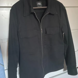 Svart jacka med dragkedja från Zara - Säljer en stilren svart jacka från Zara med dragkedja framtill och två bröstfickor. Jackan har klassisk krage och lång ärm, perfekt för en clean och enkel look. Pris ej hugget i sten!!