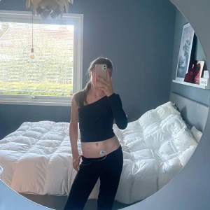 Svart oneshoulder topp - Säljer en svart, tight och croppad topp med oneshoulder-design. Toppen har en lång ärm och är tillverkad i ett stretchigt material som sitter snyggt på kroppen. Perfekt för dig som vill ha en trendig och stilren look.